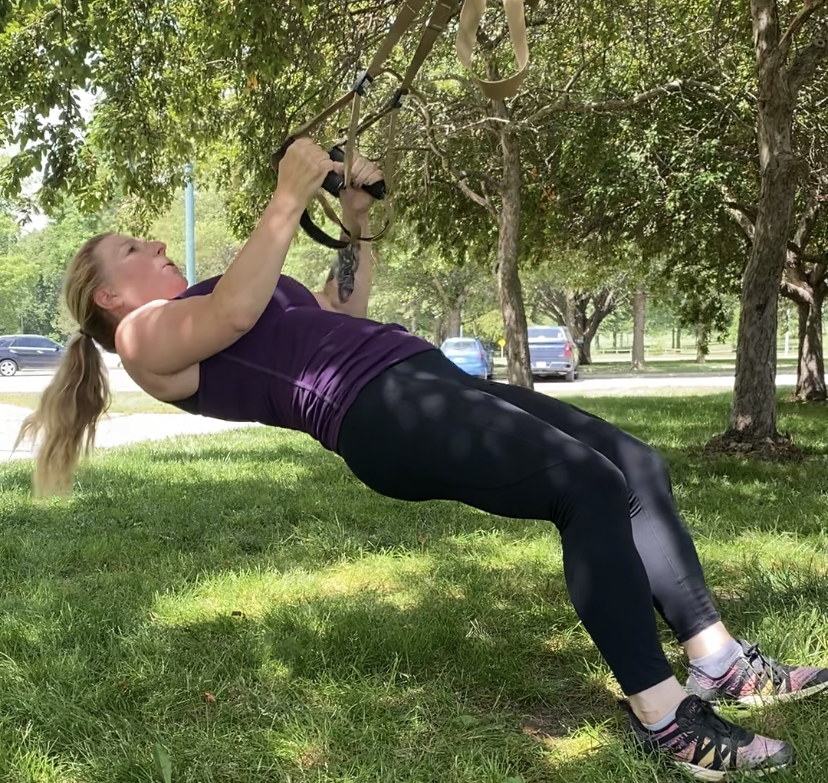 Rachel doing TRX rows suspended from a tree branch in a park